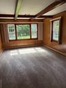 Empty room with beam ceiling, carpet flooring, wooden walls, and a baseboard heating unit