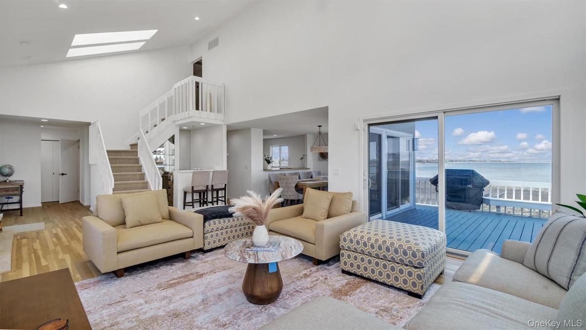Living area with high vaulted ceiling, a skylight, stairs, and a water view
