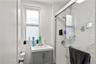 Bathroom featuring a single window, a vanity with a white countertop and gray cabinetry, and a shower enclosure with white subway tile