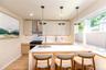 Modern kitchen featuring a waterfall island with integrated lighting, a gas range with a stainless steel range hood, and light-toned cabinetry