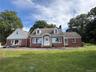 Cape cod house featuring brick siding, a front lawn, a chimney, and roof with shingles