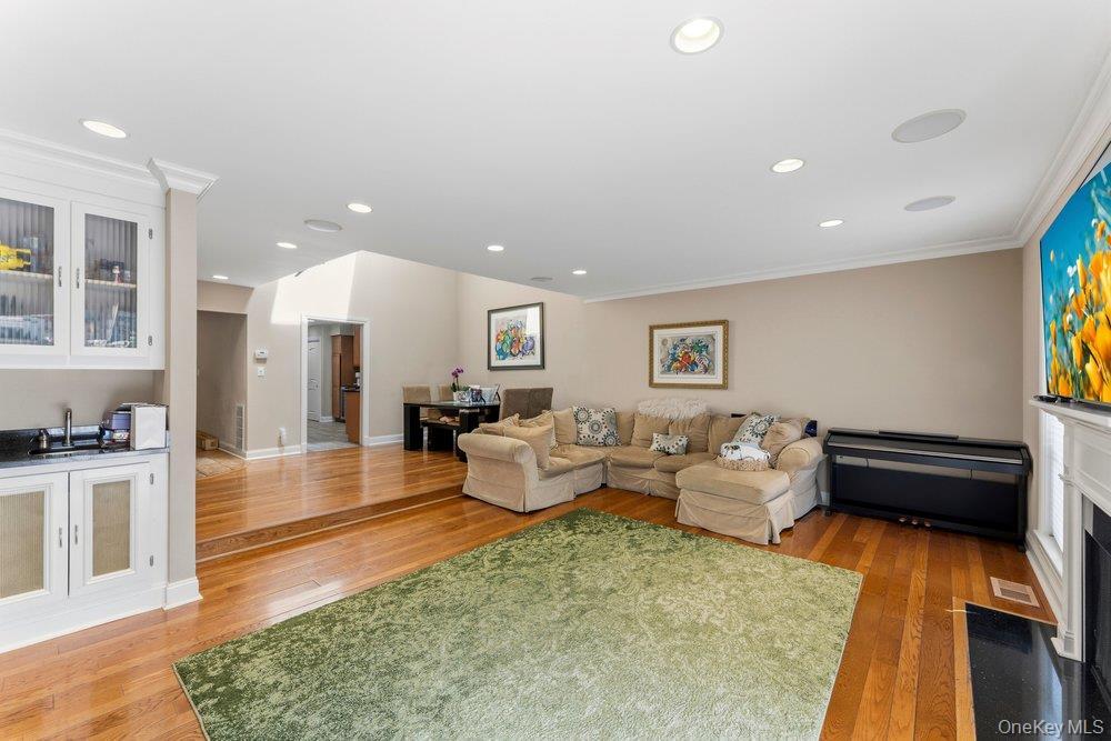 Open-concept living space featuring wood-finish flooring, a built-in wet bar with glass-front cabinetry and a dark countertop, recessed ceiling lighti