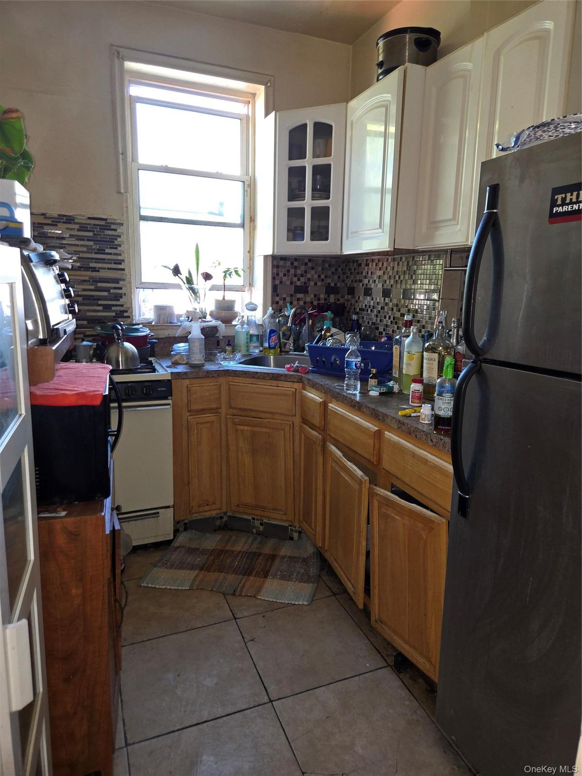 Kitchen featuring fridge, light tile patterned floors, glass insert cabinets, decorative backsplash, and brown cabinets