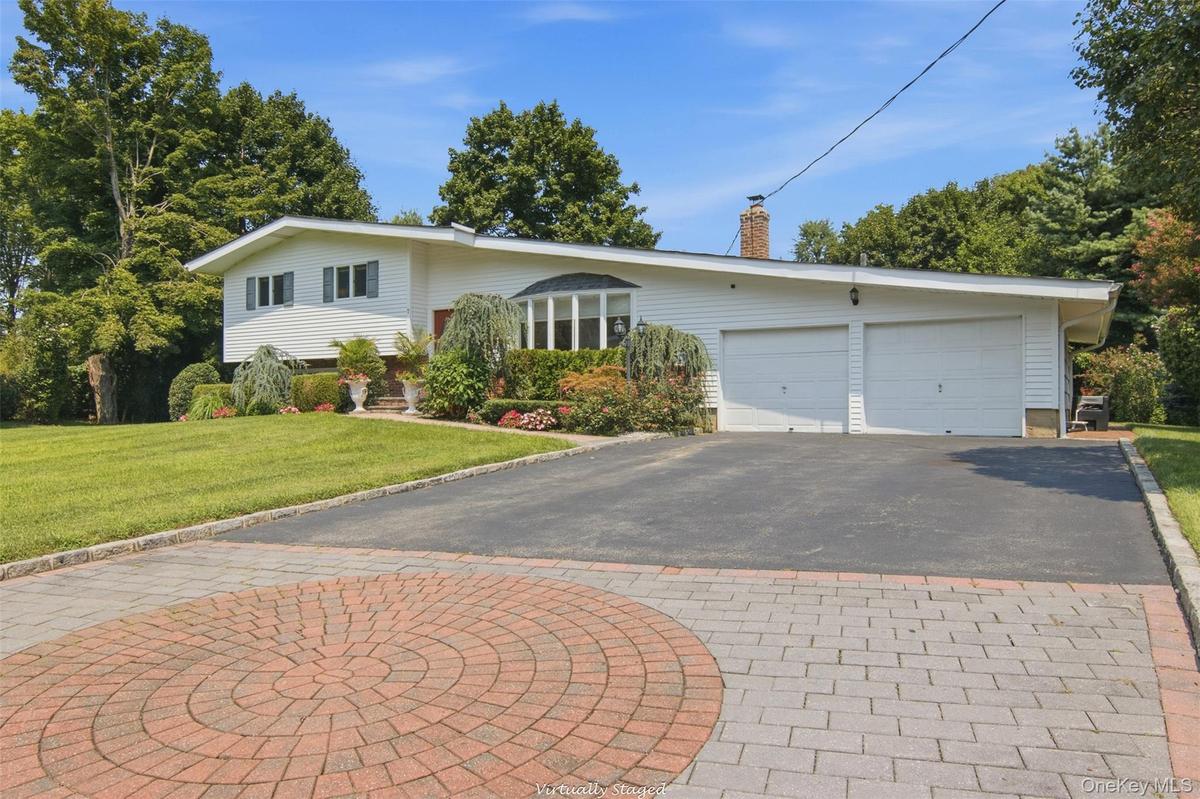 White exterior siding with dark shutters, two-car garage with white garage doors, asphalt driveway, paver stone apron, and manicured landscaping