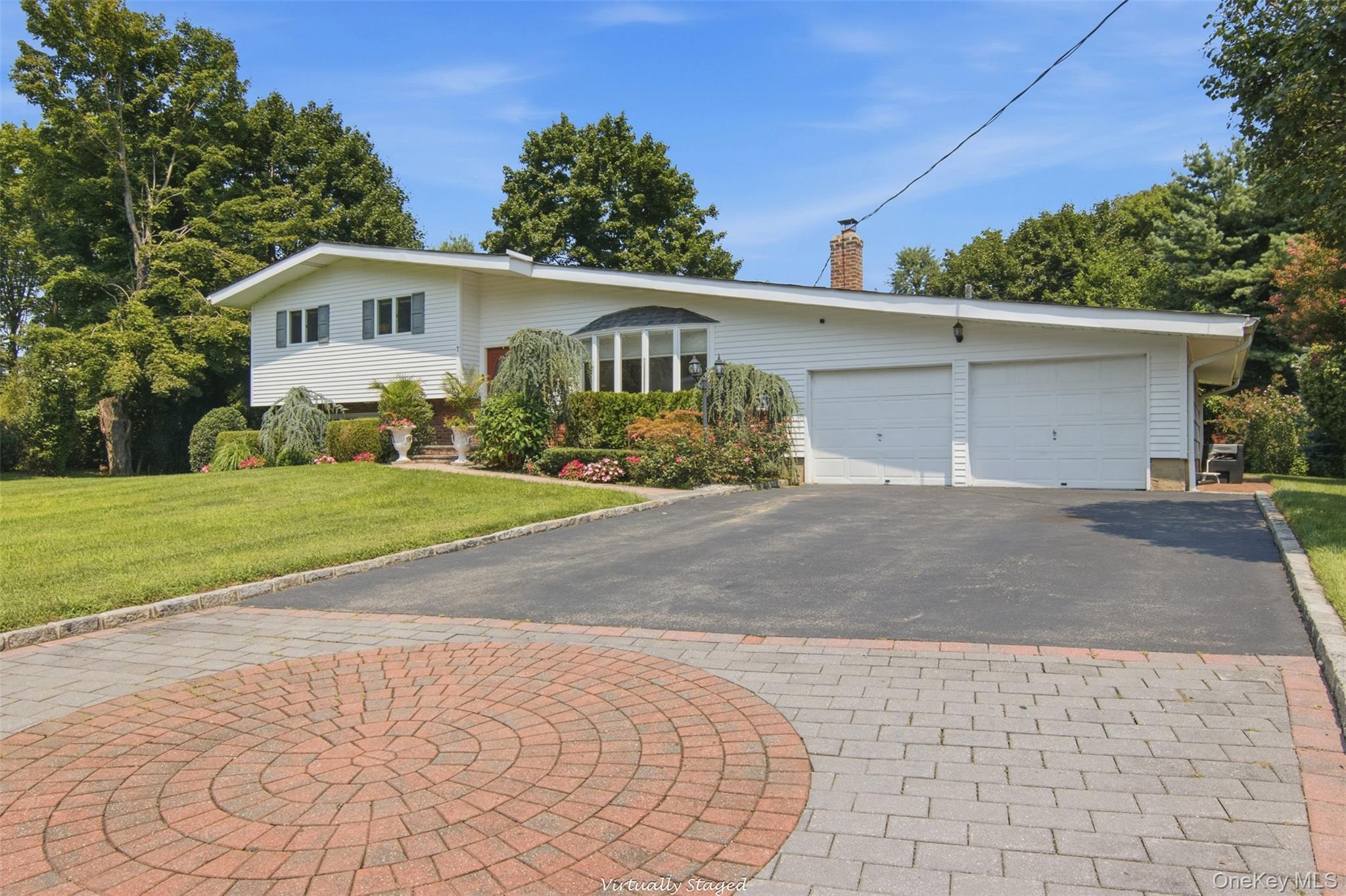 White exterior siding with dark shutters, two-car garage with white garage doors, asphalt driveway, paver stone apron, and manicured landscaping