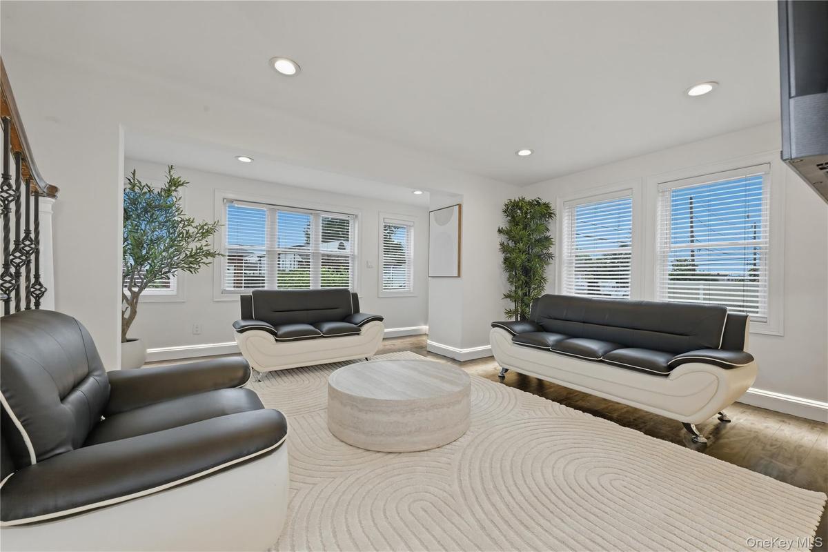 Bright interior space featuring recessed lighting, multiple windows with blinds, wood-finish flooring, and a decorative wrought iron staircase railing