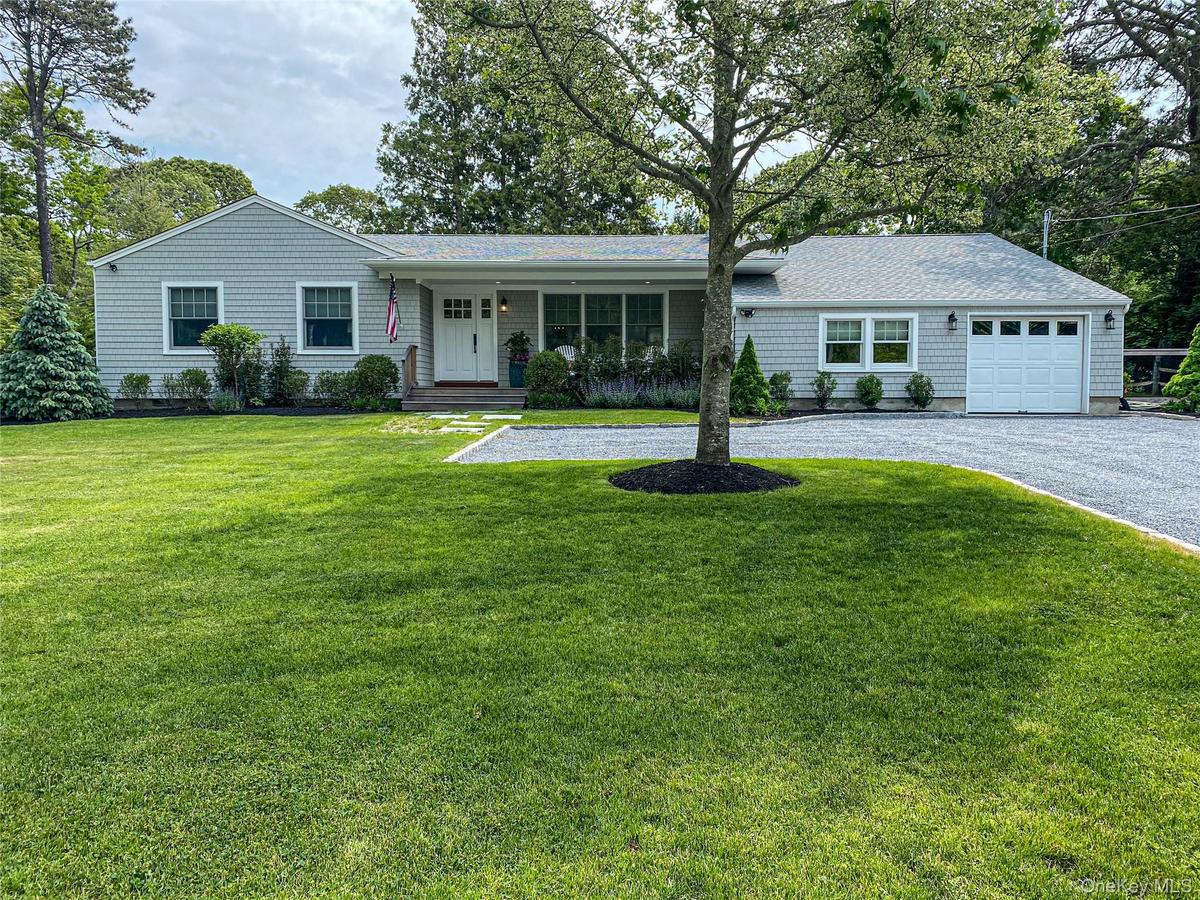 Ranch-style home with covered porch, driveway, a front lawn, an attached garage, and roof with shingles