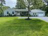 Ranch-style home with covered porch, driveway, a front lawn, an attached garage, and roof with shingles