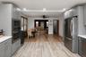 Light-toned plank flooring, gray shaker-style cabinetry, and stainless steel appliances, including a refrigerator and built-in double oven