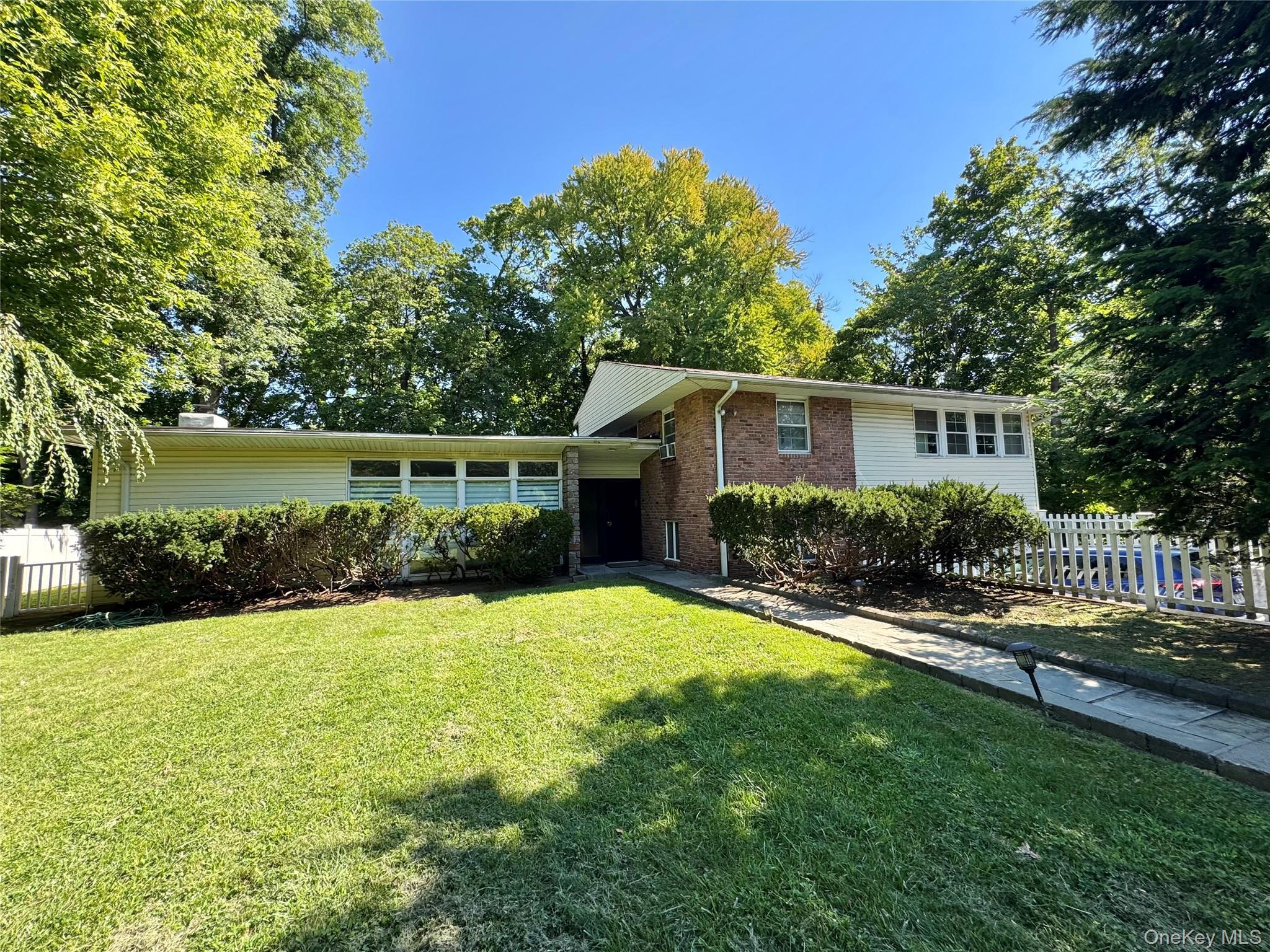 Split-level residence featuring a brick facade, white siding, and a prominent front lawn