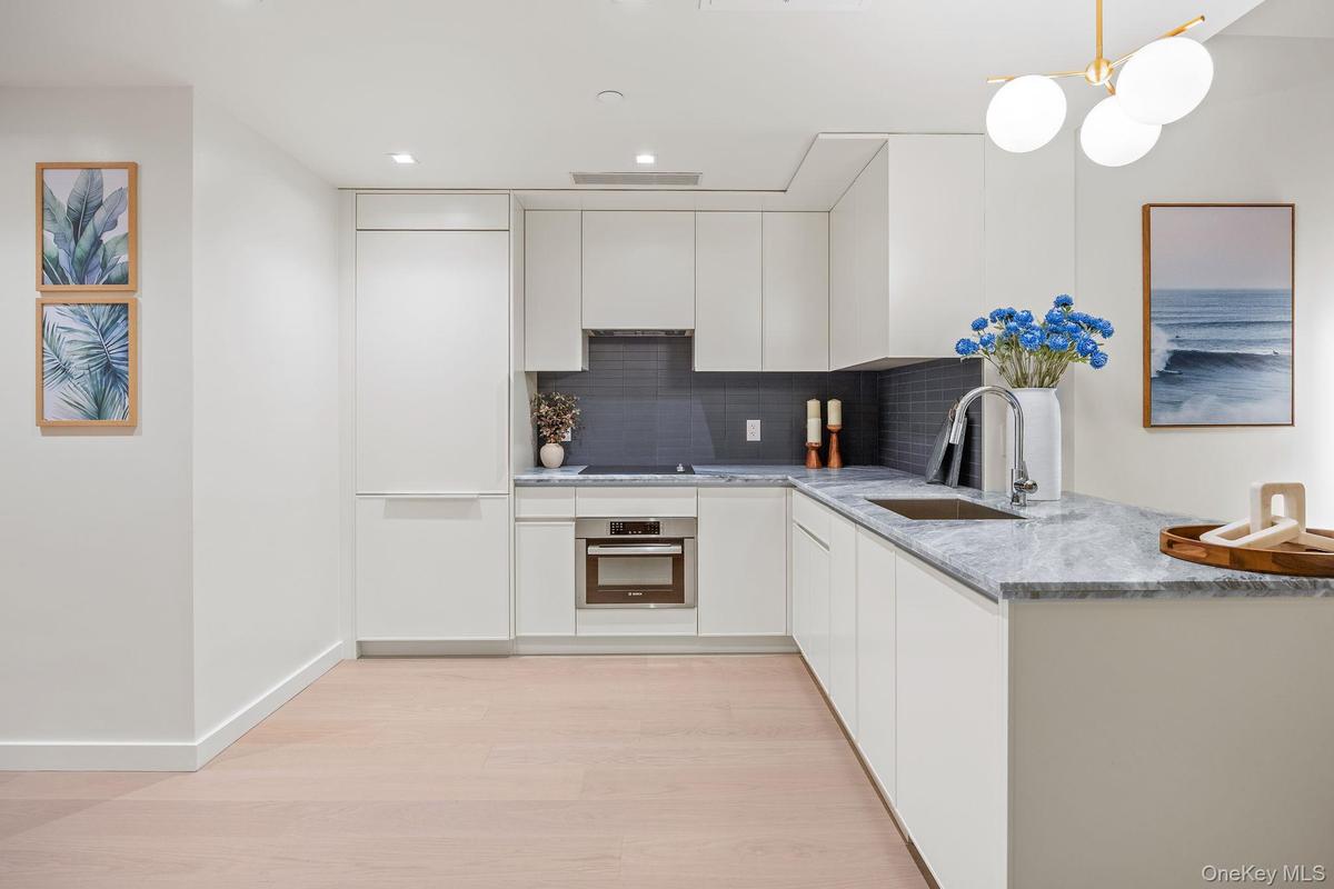 Kitchen with white cabinetry, light stone countertops, decorative backsplash, light wood-type flooring, and oven
