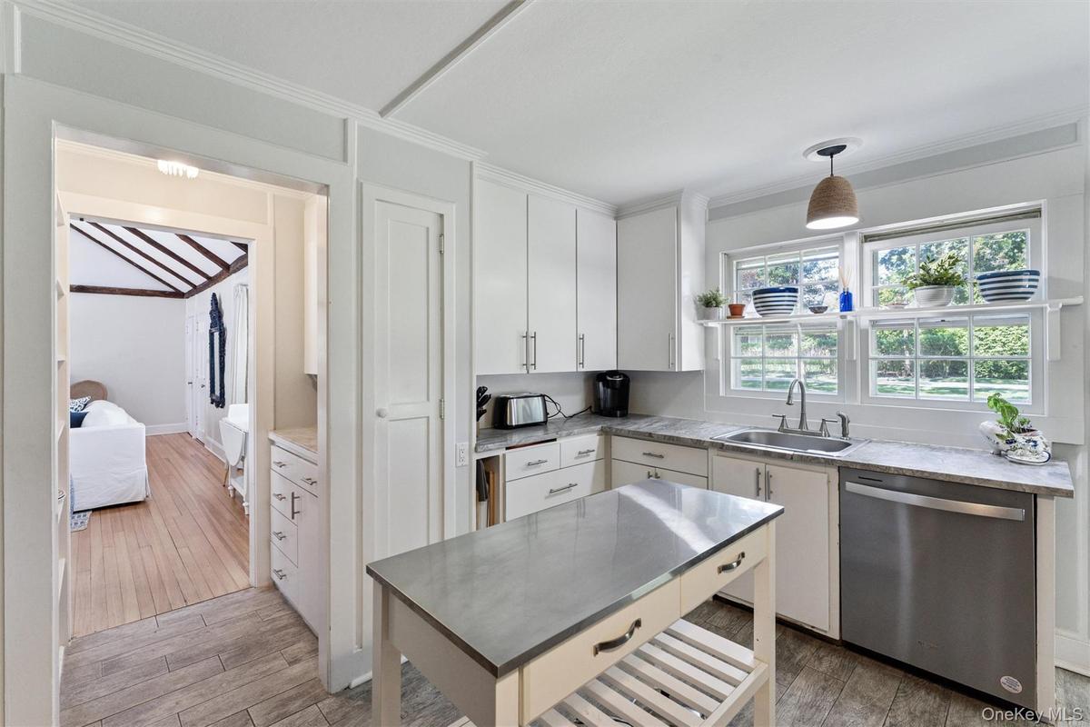 Kitchen featuring dishwasher, light wood finished floors, decorative light fixtures, white cabinetry, and ornamental molding