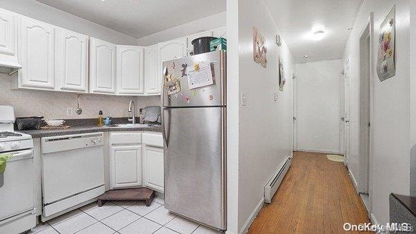 Kitchen with dark countertops, white appliances, white cabinets, a baseboard radiator, and range hood