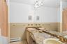Full bath with tile walls, baseboard heating, light tile patterned flooring, double vanity, and wainscoting
