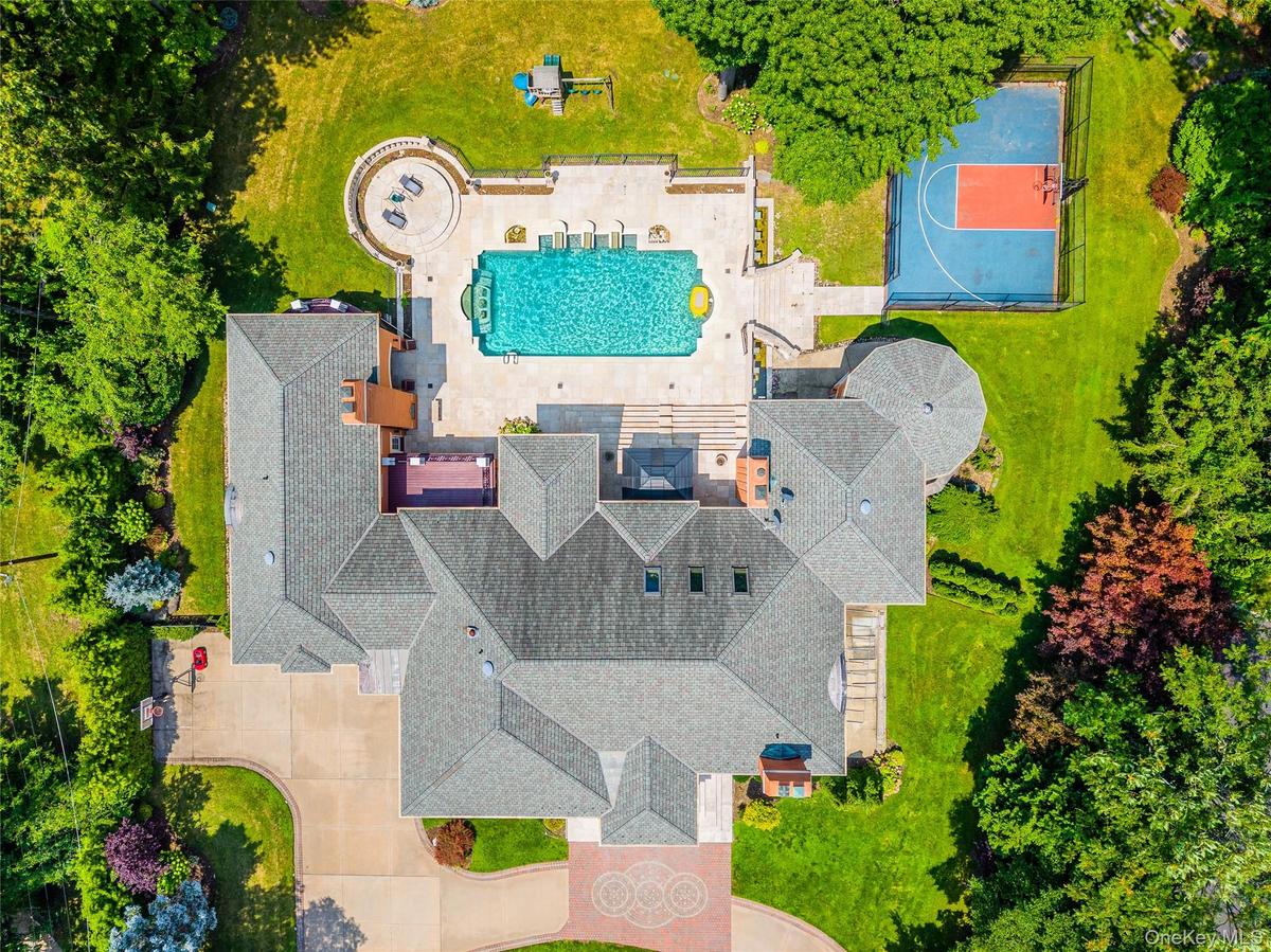 Expansive estate featuring a large swimming pool, paved patio, circular fire pit area, and a private sports court