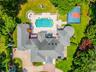 Expansive estate featuring a large swimming pool, paved patio, circular fire pit area, and a private sports court