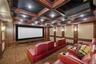 Carpeted cinema room with a decorative wall, coffered ceiling, ornamental molding, and beamed ceiling