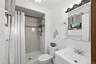 Bathroom featuring a stand-up shower with tiled walls and decorative accent band, white vanity with integrated sink, chrome faucet, wall-mounted mirro