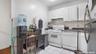 Kitchen featuring white appliances, white cabinetry, dark countertops, light tile patterned flooring, and under cabinet range hood