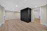 Spacious room with light wood-finish flooring, a painted brick feature, recessed lighting, and a doorway to an additional room with wood-finish floori