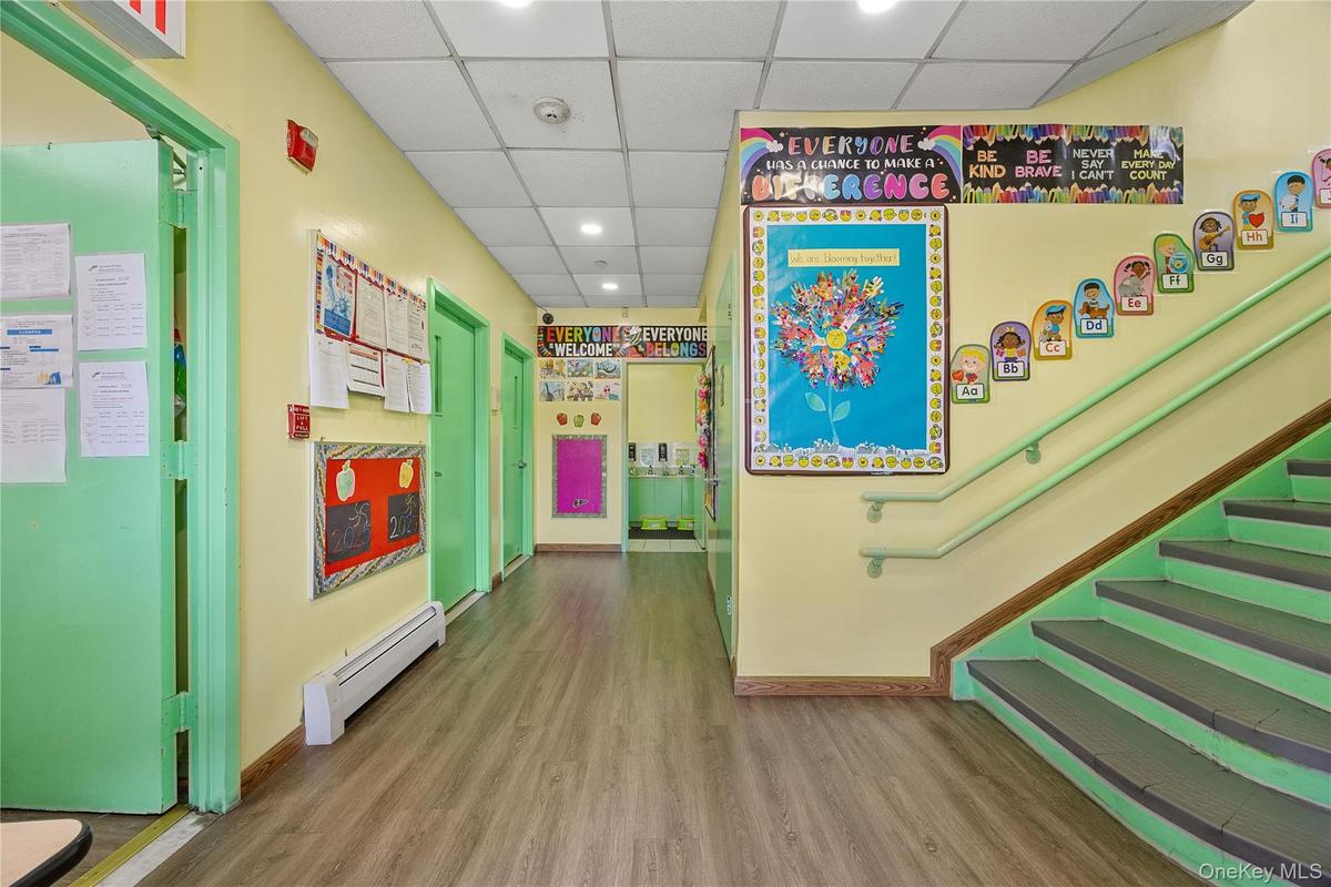 Corridor featuring a paneled ceiling, wood finished floors, a baseboard heating unit, recessed lighting, and stairs