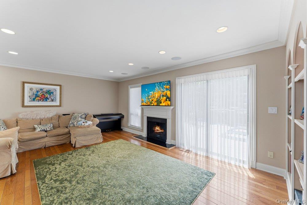 Hardwood flooring throughout featuring a fireplace with a white mantel and dark hearth, built-in recessed lighting, crown molding, and a sliding glass