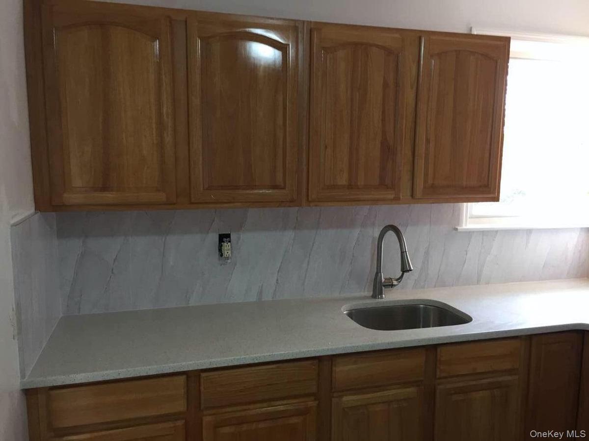 Kitchen featuring a sink, tasteful backsplash, brown cabinets, and light stone countertops