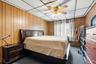 Carpeted bedroom featuring a drop ceiling, wood walls, and a ceiling fan