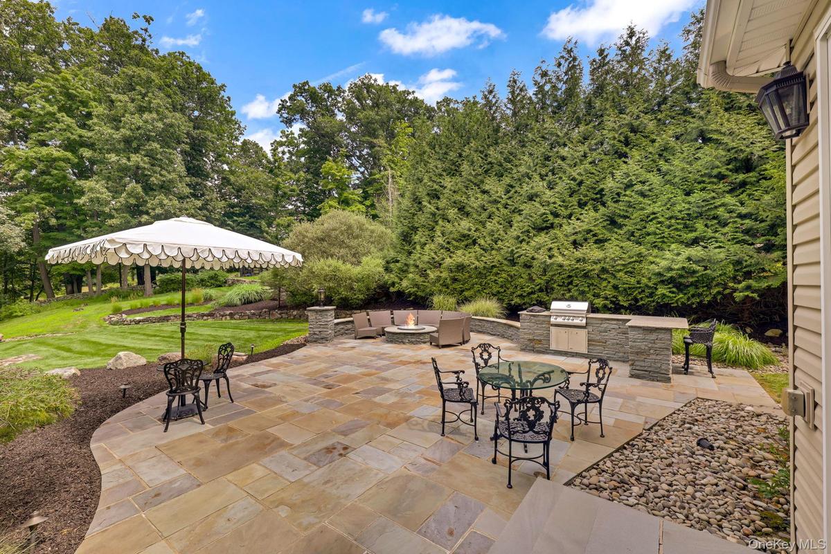 Expansive stone patio with a built-in outdoor kitchen, integrated fire pit, and stone retaining wall