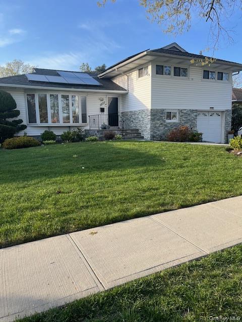 White siding exterior with a stone veneer accent, bay window, solar panels, and attached garage