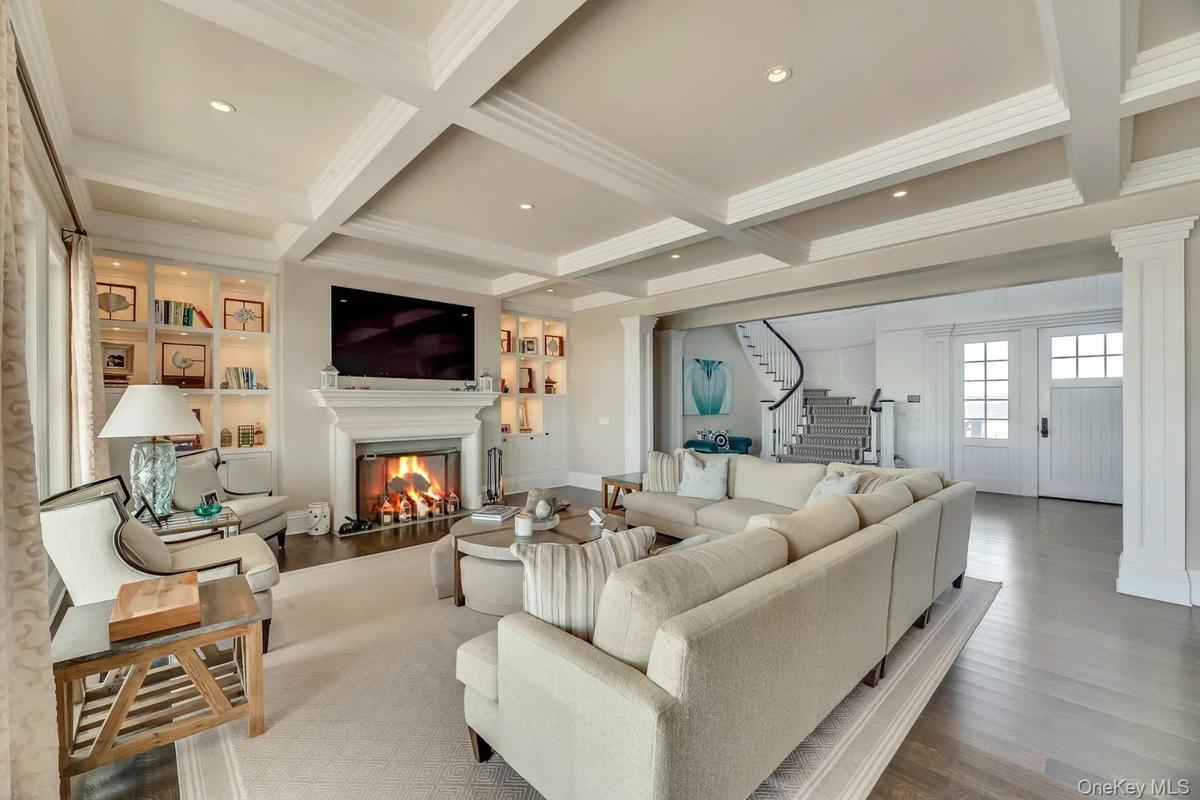 Living area with wood finished floors, beamed ceiling, a glass covered fireplace, stairs, and coffered ceiling