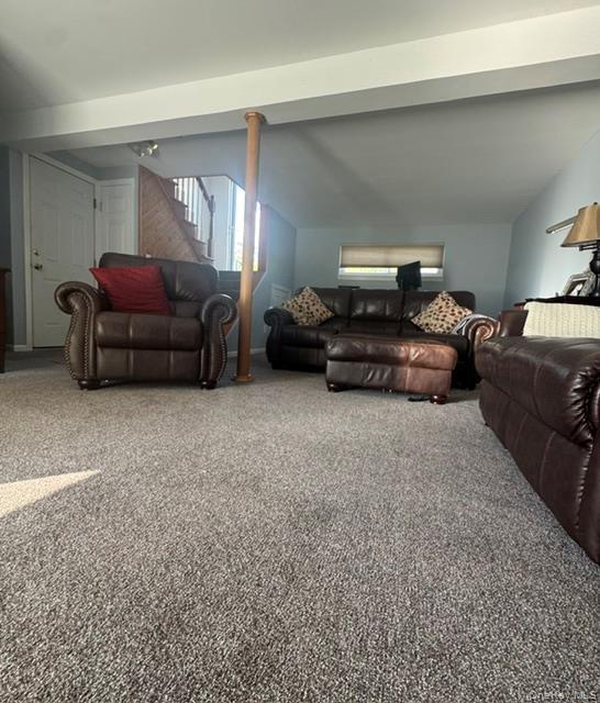 Spacious room featuring neutral carpeting, a staircase with wood-finish railing, and a light-toned ceiling with exposed beam