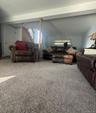 Spacious room featuring neutral carpeting, a staircase with wood-finish railing, and a light-toned ceiling with exposed beam