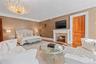 Spacious room featuring a prominent fireplace with a stone surround and white mantel, a large decorative chandelier, light wood-finish flooring, and a