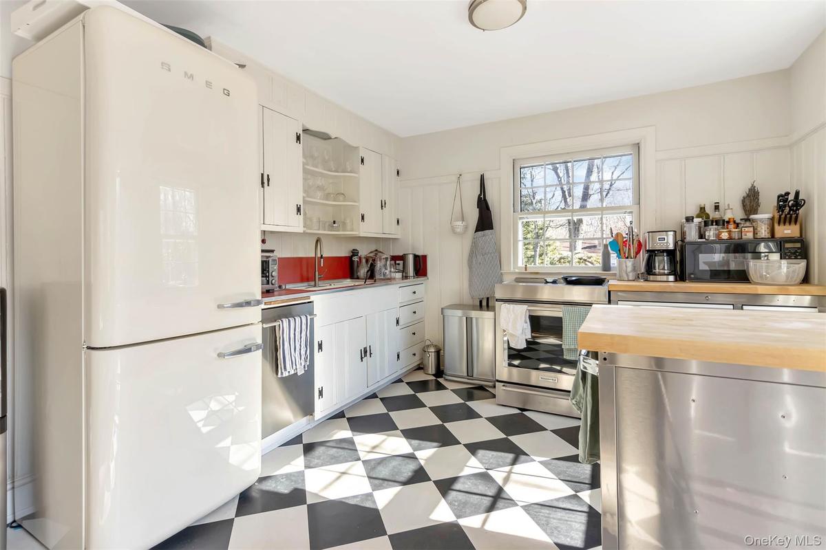 Kitchen with a sink, wood counters, white cabinetry, appliances with stainless steel finishes, and light floors