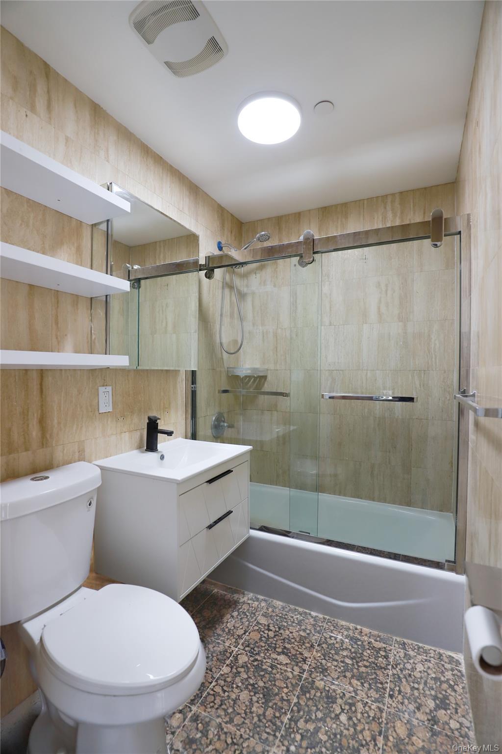 Bathroom featuring vanity, combined bath / shower with glass door, and tile walls