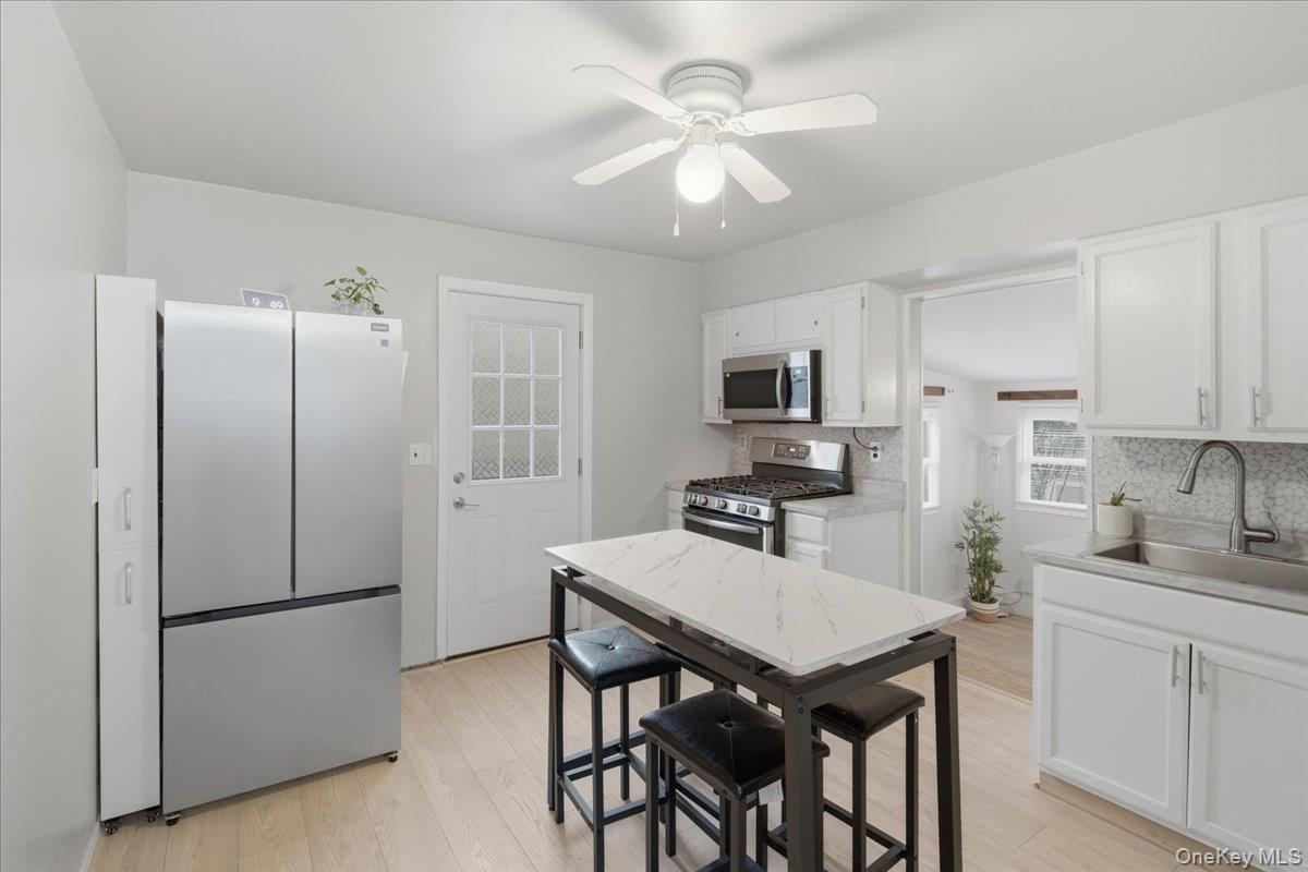 Kitchen featuring appliances with stainless steel finishes, white cabinets, decorative backsplash, light wood-style flooring, and a ceiling fan