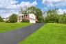 Greek revival house featuring a chimney, driveway, a garage, brick siding, and a front yard