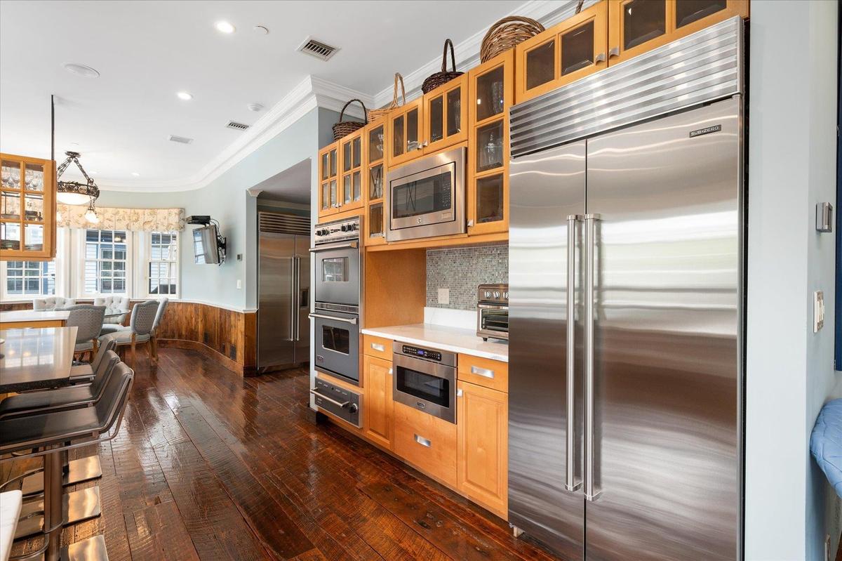 Kitchen featuring wainscoting, built in appliances, crown molding, dark wood-style floors, and light countertops