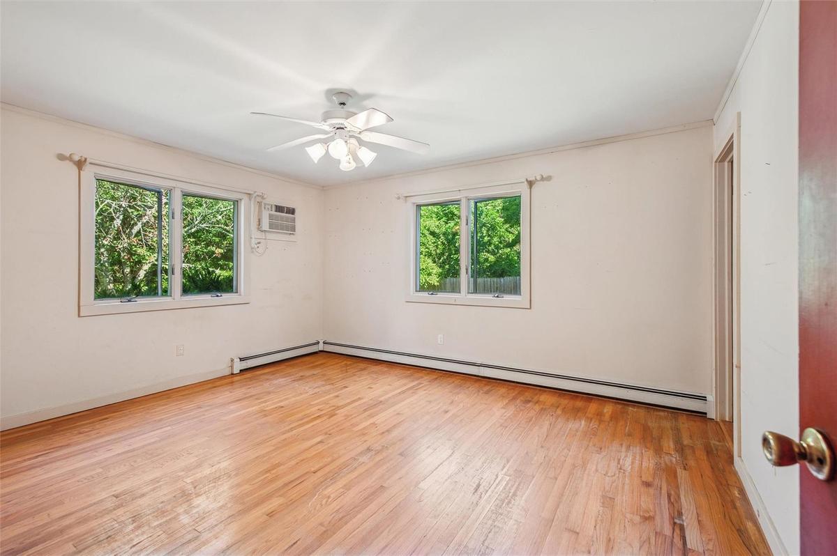 Empty room with healthy amount of natural light, a baseboard radiator, hardwood / wood-style floors, a wall unit AC, and crown molding