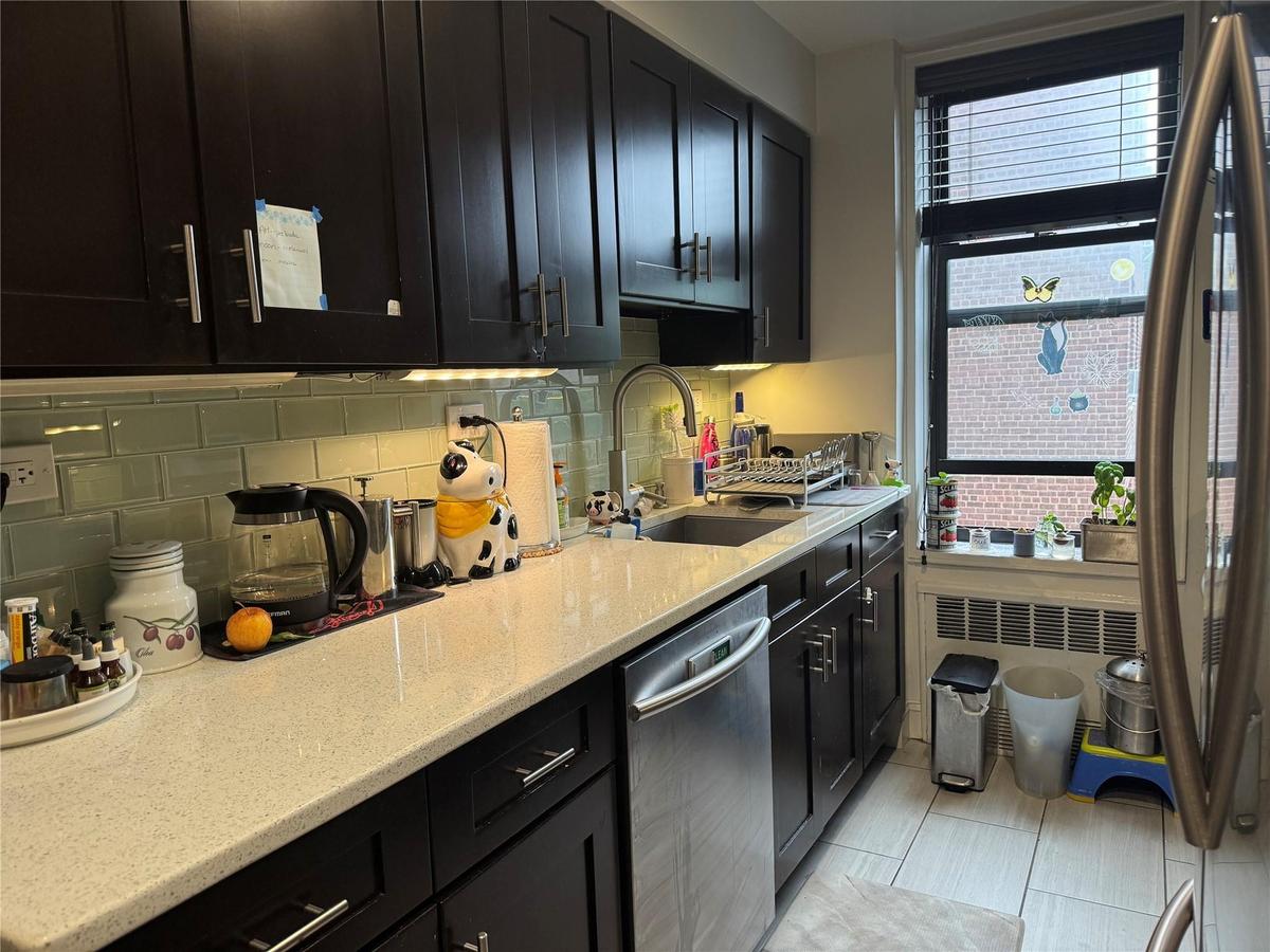 Kitchen with stainless steel dishwasher, dark cabinets, backsplash, and light stone counters
