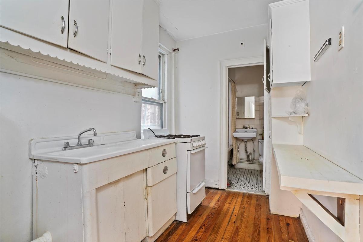 Kitchen with white gas stove, dark wood-style floors, light countertops, and white cabinets