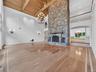Unfurnished living room with a chandelier, high vaulted ceiling, arched walkways, wood finished floors, and a stone fireplace