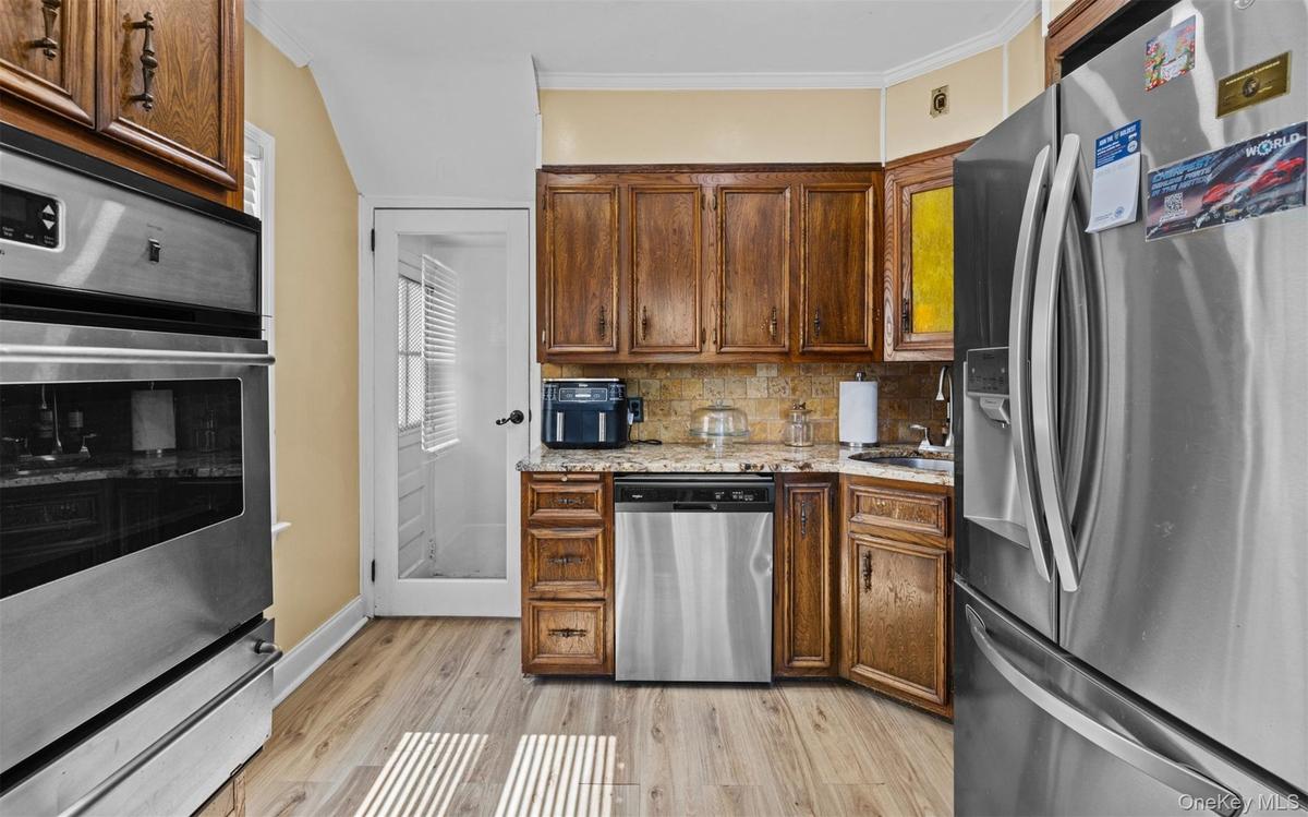 Kitchen featuring appliances with stainless steel finishes, decorative backsplash, light wood finished floors, ornamental molding, and a warming drawe