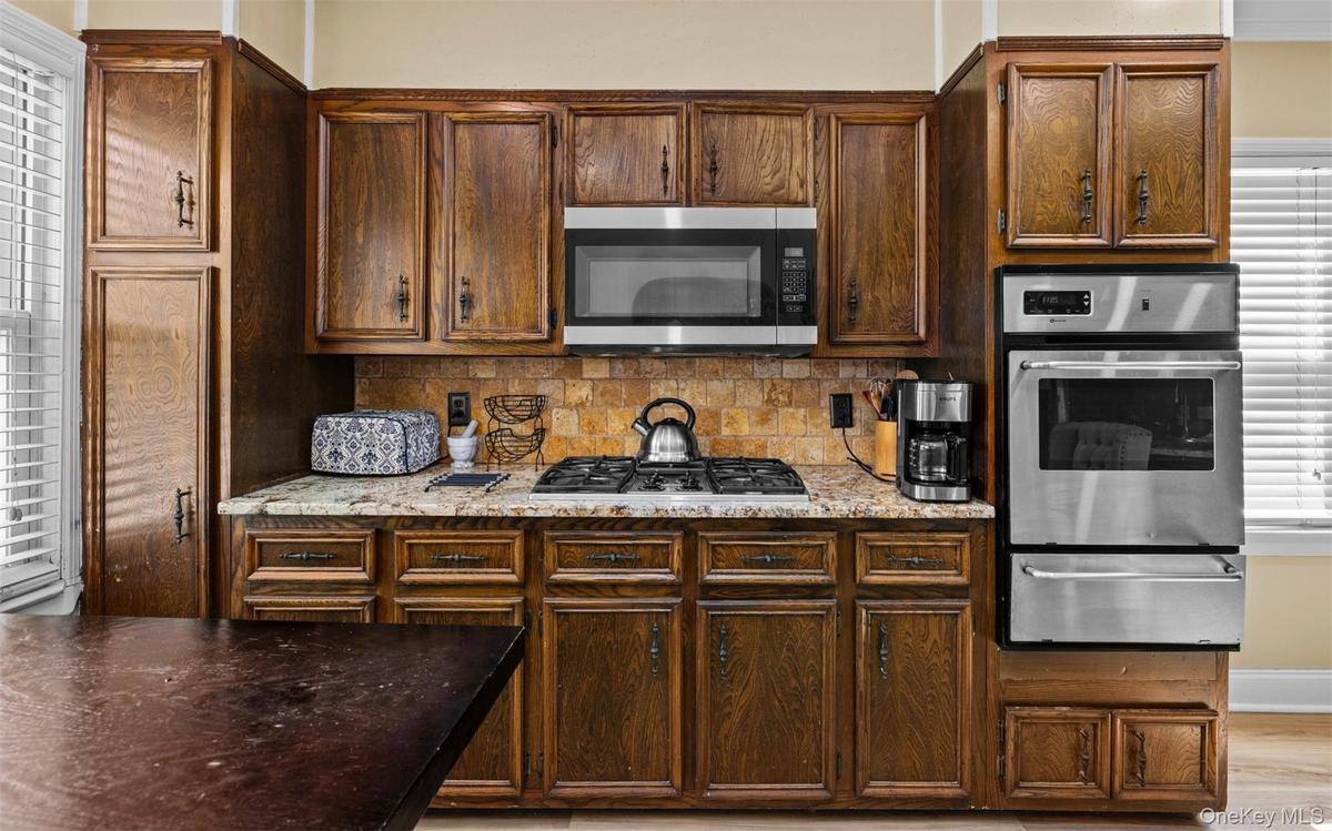 Kitchen with stainless steel appliances, backsplash, a warming drawer, light stone countertops, and light wood-type flooring