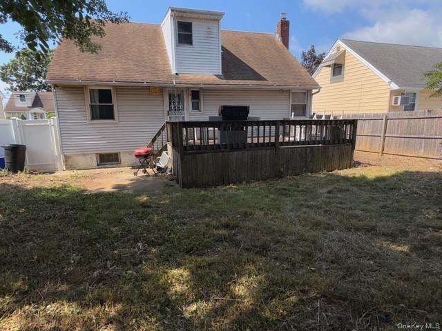 Rear view of house featuring a fenced backyard, a deck, a chimney, and a shingled roof