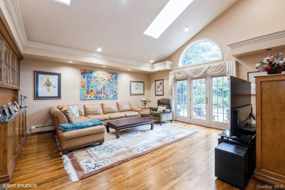 Living room with high vaulted ceiling, a skylight, recessed lighting, light wood-style flooring, and a baseboard radiator