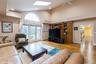 Living room featuring high vaulted ceiling, light wood finished floors, a skylight, a baseboard heating unit, and a ceiling fan