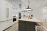 kitchen breakfast bar, white cabinets, an island with sink, light stone counters, and hanging light fixtures