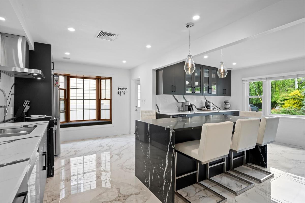 Kitchen with light marble finish flooring, recessed lighting, glass insert cabinets, pendant lighting, and wall chimney exhaust hood